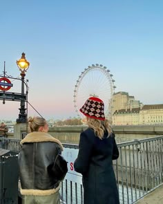 two women are standing on a bridge looking at the ferris wheel in london, england