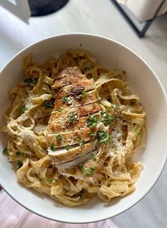 a white bowl filled with pasta covered in meat and parsley on top of a table