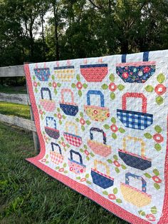 a quilt hanging on the side of a fence in front of some trees and grass