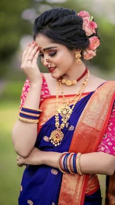 a woman in a blue and red sari with gold jewelry on her neck, holding her hand to her face