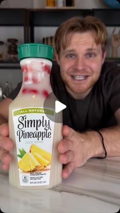 a man holding up a bottle of simply pineapple smoothie on a counter top