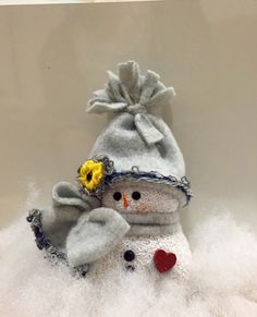 a stuffed snowman with a yellow flower in its hat and scarf on top of some white fluffy material