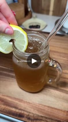 a person holding a lemon wedge over a cup of tea on a wooden counter top