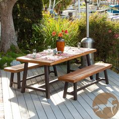 a picnic table with an umbrella over it on a deck next to flowers and trees