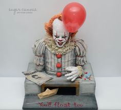 a statue of a clown with a red balloon on it's head sitting at a table