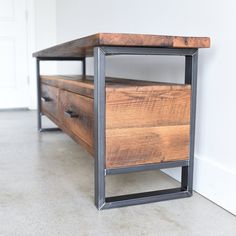 a wooden table with metal frame and drawers on the bottom, against a white wall