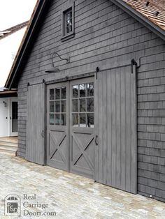 a gray barn with two doors and windows