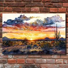 a painting hanging on a brick wall with a cactus in the foreground and sunset in the background