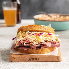 a sandwich with meat and coleslaw on a cutting board next to a glass of beer