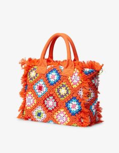 an orange handbag with flowers and fringes on the front, sitting against a white background