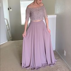 a woman standing in a room wearing a long purple skirt and off the shoulder top