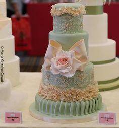 three tiered wedding cake with flowers on each layer and ribbons at the top, sitting on a table