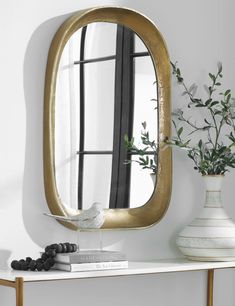 a white table with a vase and mirror on it next to a wall mounted bird