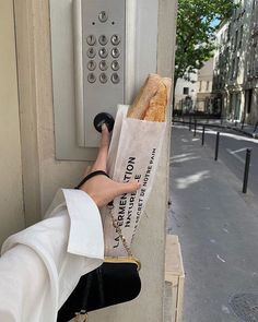 a person is holding a baguette in front of an atm machine on the street