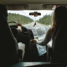 two people sitting in the back seat of a car looking at a map and drinking wine