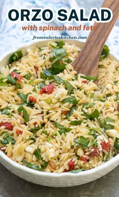 a white bowl filled with pasta and spinach on top of a table next to a wooden spoon