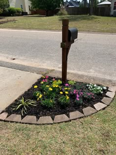 a mailbox in the middle of a flower bed with flowers growing out of it