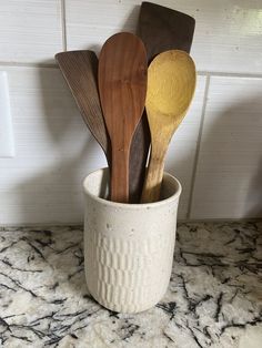 several wooden spoons in a white cup on a marble counter