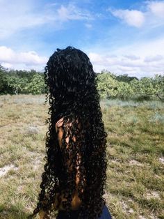 the back of a woman's head with long curly hair sitting in a field