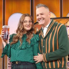 a man and woman standing next to each other in front of a tv screen holding drinks