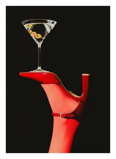 a martini glass with olives in it sitting on top of a red stand that is shaped like a vase