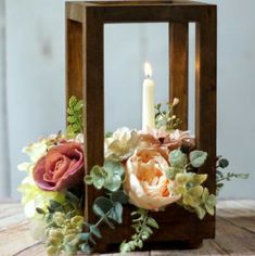 a small wooden lantern with flowers and candles in it on top of a wood table