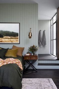 there is a bed with green sheets and pillows on the floor next to a wooden table