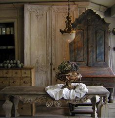 an old wooden table sitting in front of a dresser and armoire with flowers on it