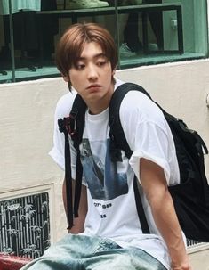 a young man sitting on top of a skateboard in front of a building and looking at the camera