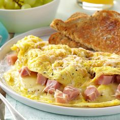 an omelet with ham and cheese is on a white plate next to toast