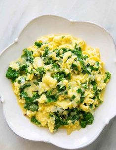 scrambled eggs with spinach and cheese in a white bowl on a marble countertop