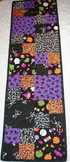 a purple and black patchwork table runner with halloween decorations on the edges, along with pumpkins