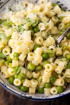 a bowl filled with pasta, peas and parmesan cheese on top of a wooden table