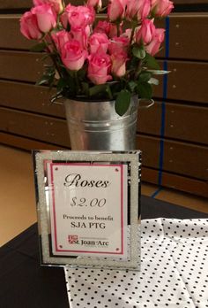 pink roses are in a metal bucket on a table with a price sign for $ 2 00