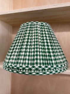 a green and white gingham lamp shade hanging from a wooden shelf in a room