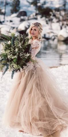 a woman standing in the snow holding a bouquet and wearing a dress with long sleeves