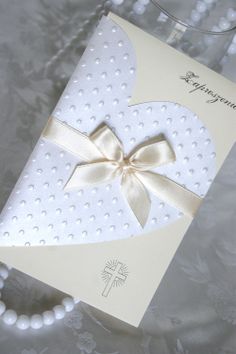 a white card with a gold bow on it next to a pearl necklace and bracelet