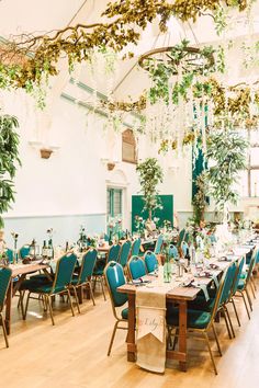 a dining room set up for an event with blue chairs and greenery hanging from the ceiling