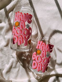 two glasses that have been decorated with pink and orange letters on them, sitting on a white sheet