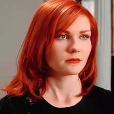 a woman with red hair and blue eyes wearing a black shirt is looking at the camera