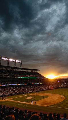 the sun is setting over a baseball field as storm clouds loom in the background