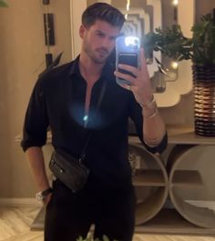 a man taking a selfie with his cell phone in front of him and wearing black pants