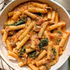 a white bowl filled with pasta and sauce on top of a table next to a napkin