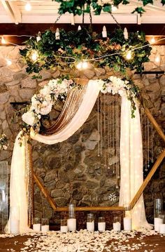 a stone wall with candles and flowers on it is decorated with greenery for an outdoor wedding