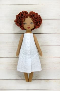 a doll with red hair wearing a white dress and standing on a wooden floor next to wood planks