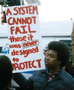 a protester holds up a sign that reads a system cannot fail those it was never designed to protect