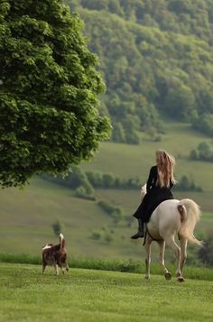 a woman riding on the back of a white horse next to a dog