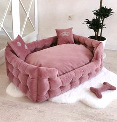 a pink dog bed sitting on top of a white rug next to a potted plant