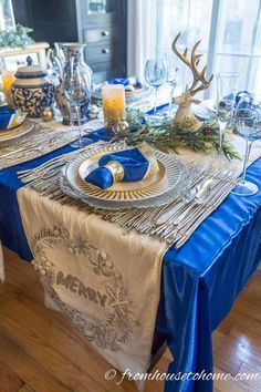 the table is set with silverware and blue linens for an elegant christmas dinner