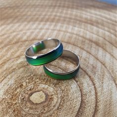 two wedding rings sitting on top of a wooden table next to each other, one green and the other silver